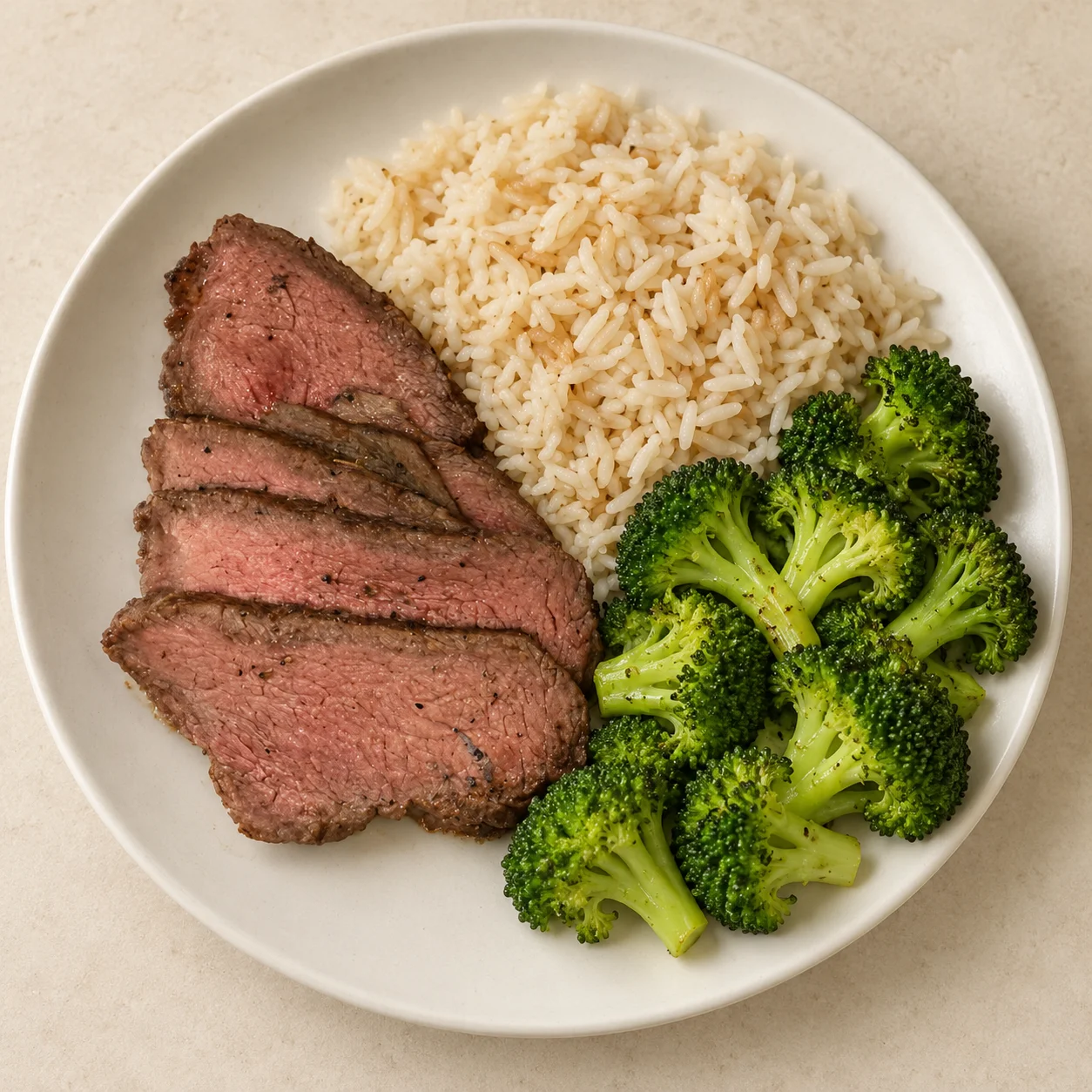 Sliced grass-fed sirloin with jasmine rice and steamed broccoli on a white plate.