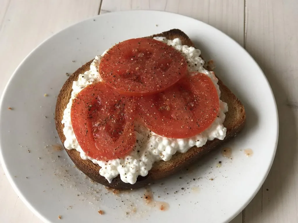 An open-face cottage cheese toast topped with sliced tomato, everything bagel seasoning, basil, and balsamic glaze.